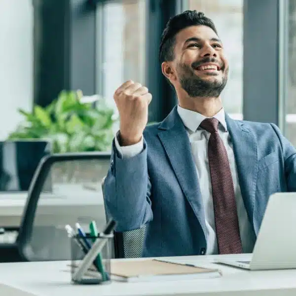 Happy businessman looking up and showing winner gesture while sittin