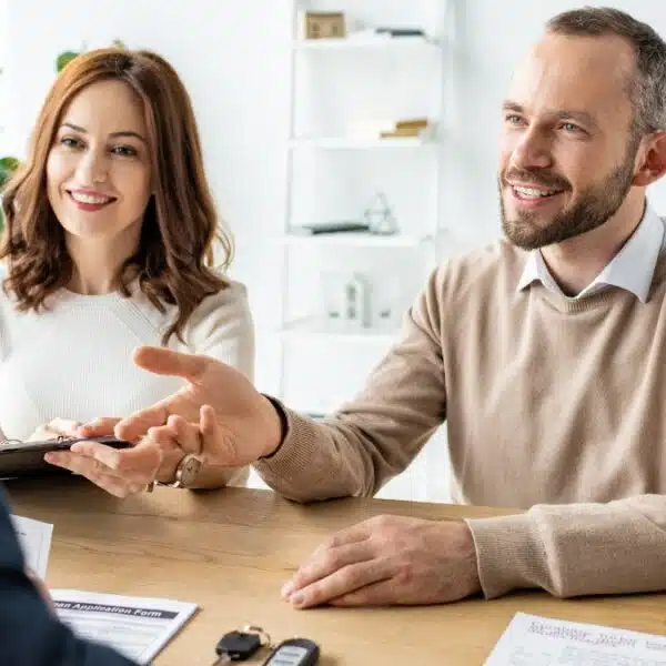 Happy man gesturing near woman with clipboard and car dealer