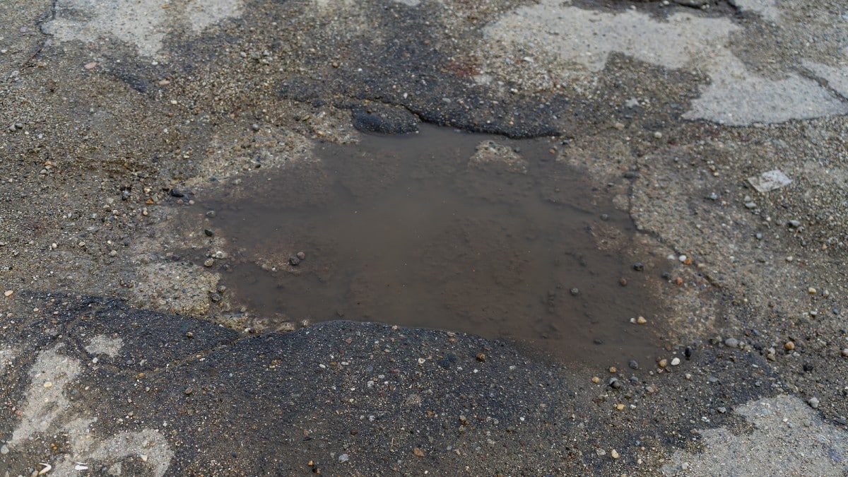 14 Signs Your Neighborhood May Be Losing Value Damaged-asphalt-pavement-road-with-pothole.-Pothole-with-rainwat