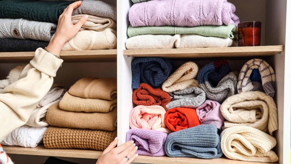 20 Things Minimalists Refuse to Spend Money On Woman-taking-warm-sweater-from-shelf-in-wardrobe-closeup