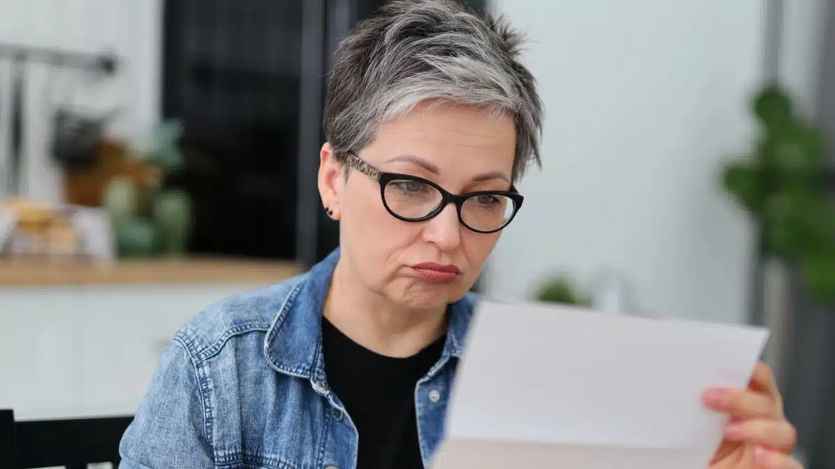 mature woman glasses reading mail sad