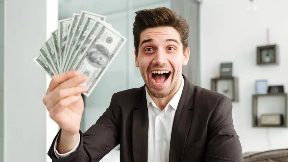 man holding cash in front of a laptop