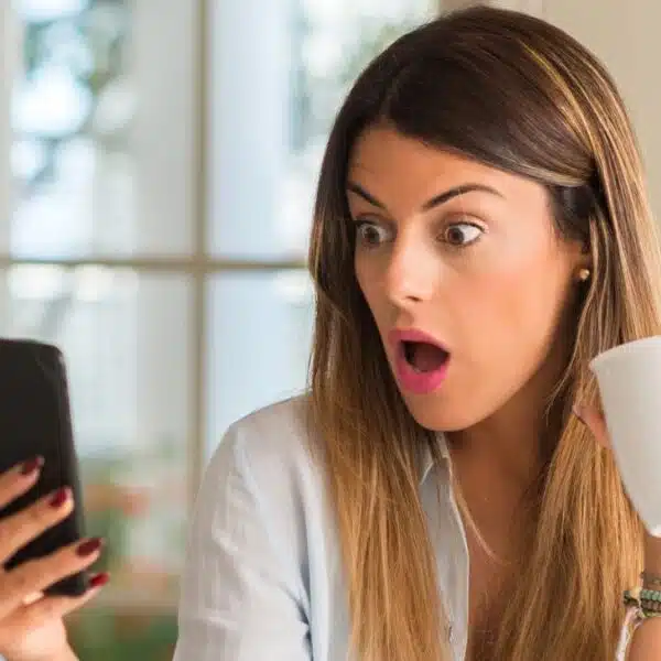 woman staring at her phone in shock at home
