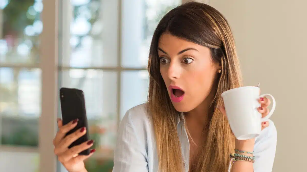 woman staring at her phone in shock at home