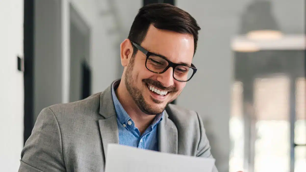 man glasses reviewing documents with laptop